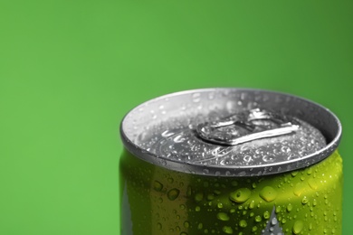 Photo of Aluminum can of beverage covered with water drops on green background, closeup. Space for text