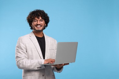 Smiling man with laptop on light blue background, space for text