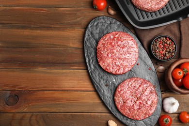 Photo of Raw hamburger patties with pepper and vegetables on wooden table, flat lay. Space for text