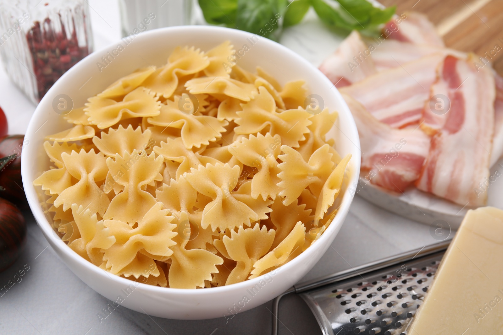 Photo of Raw pasta, bacon and fresh ingredients on white tiled table