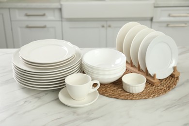 Photo of Clean plates, bowls and cup on white marble table in kitchen