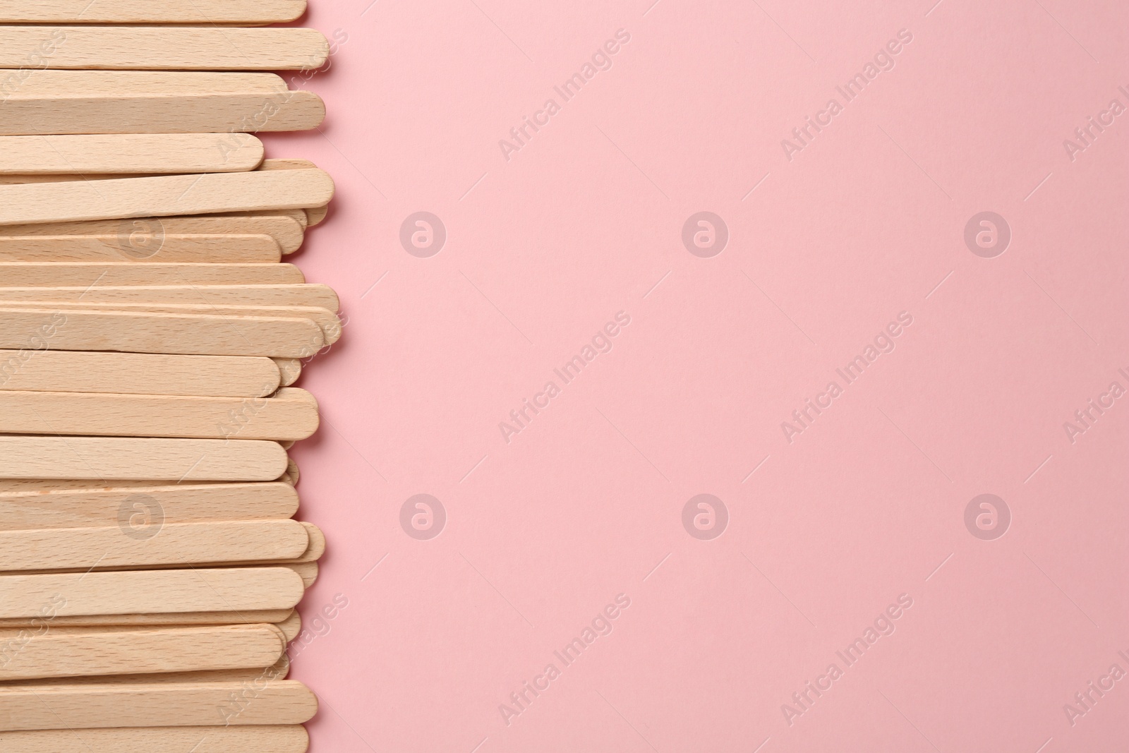 Photo of Wooden waxing spatulas on light pink background, flat lay. Space for text