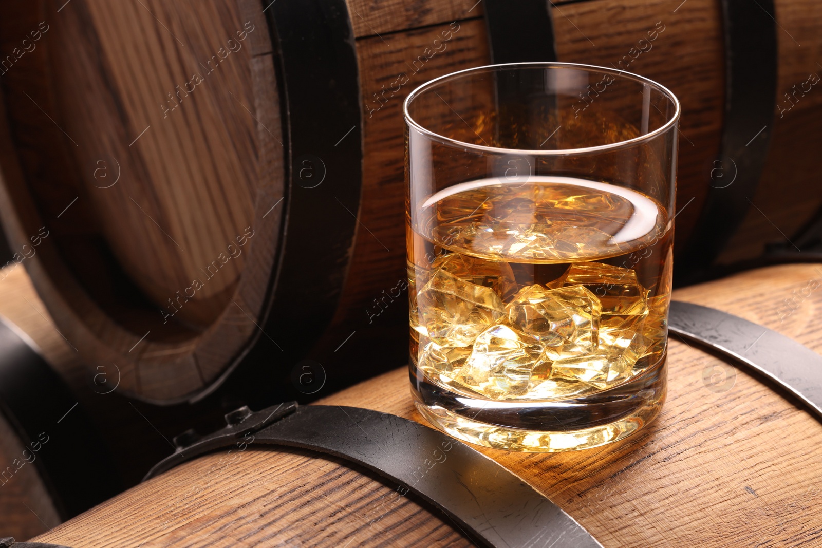 Photo of Whiskey with ice cubes in glass on wooden barrel, closeup