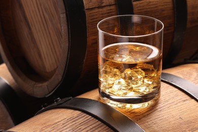 Whiskey with ice cubes in glass on wooden barrel, closeup