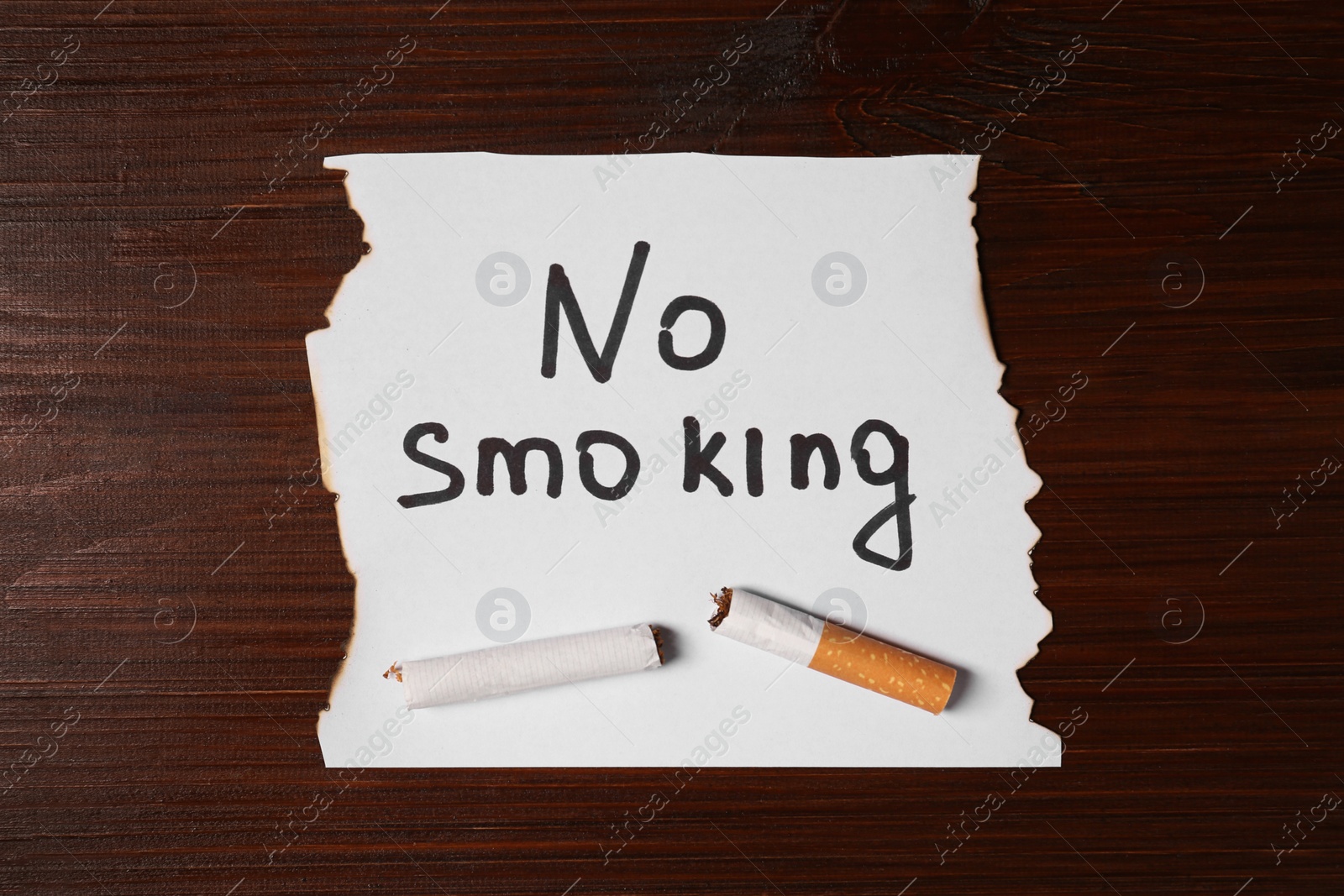 Photo of Broken cigarette and words No Smoking written on paper on wooden table, top view