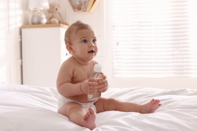 Cute little baby with bottle of massage oil on bed at home