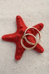 Honeymoon concept. Two golden rings and sea star on sand, top view