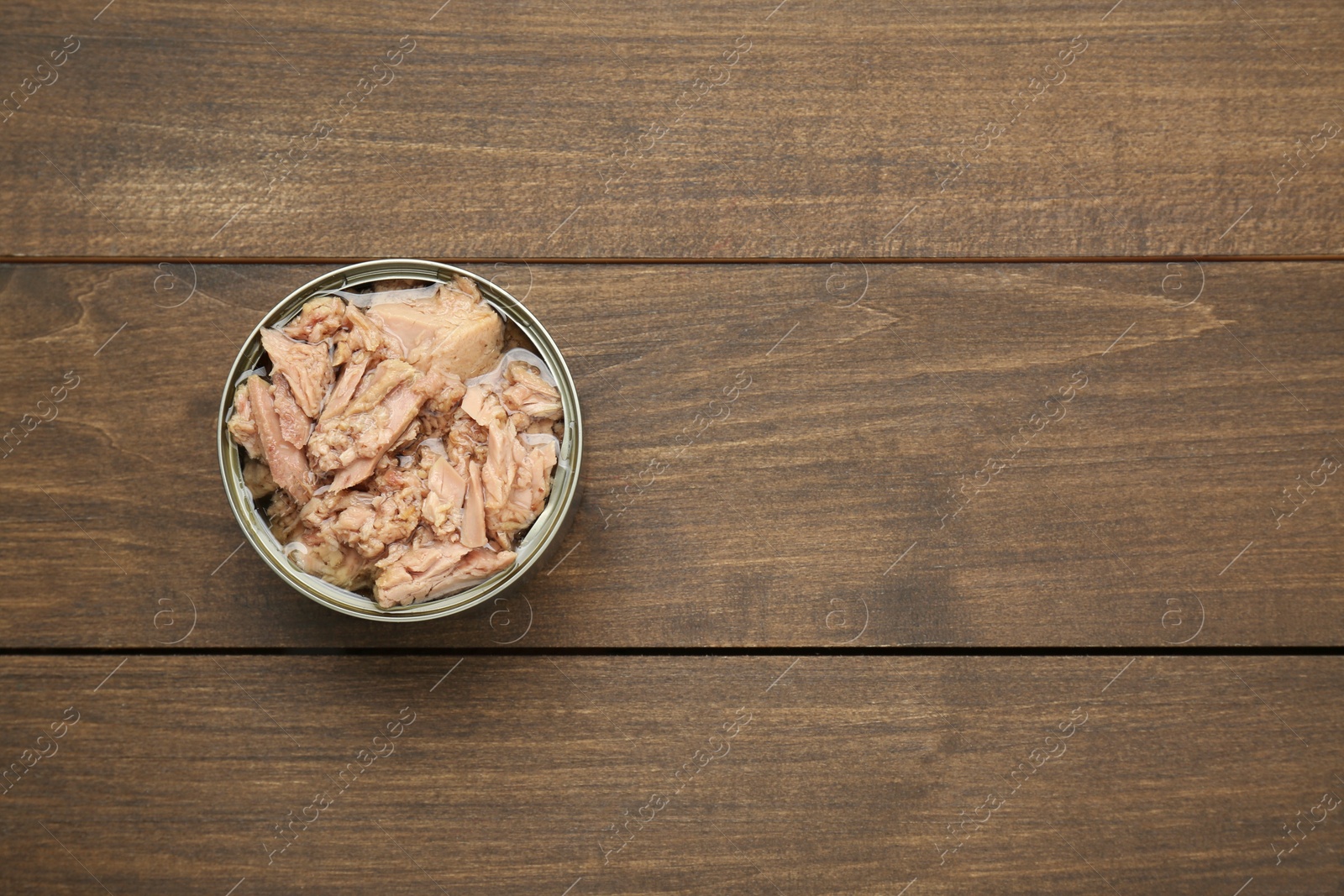 Photo of Tin can with canned tuna on wooden table, top view. Space for text