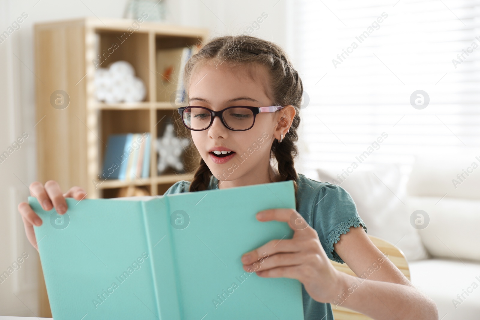 Photo of Cute little girl reading book at home