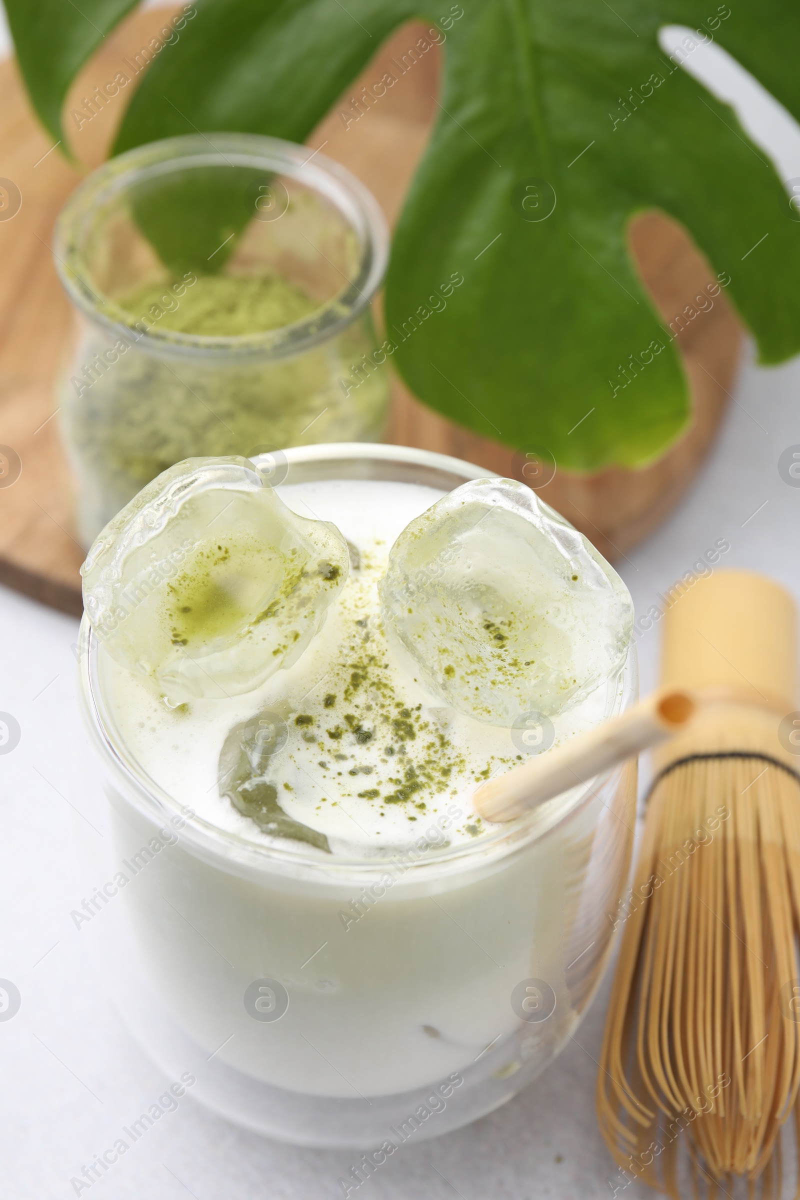 Photo of Glass of tasty iced matcha latte, leaf and bamboo whisk on white table