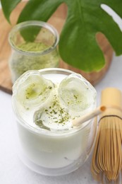 Glass of tasty iced matcha latte, leaf and bamboo whisk on white table