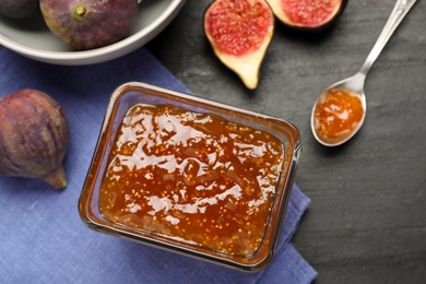 Delicious fig jam and fresh fruits on black table, flat lay