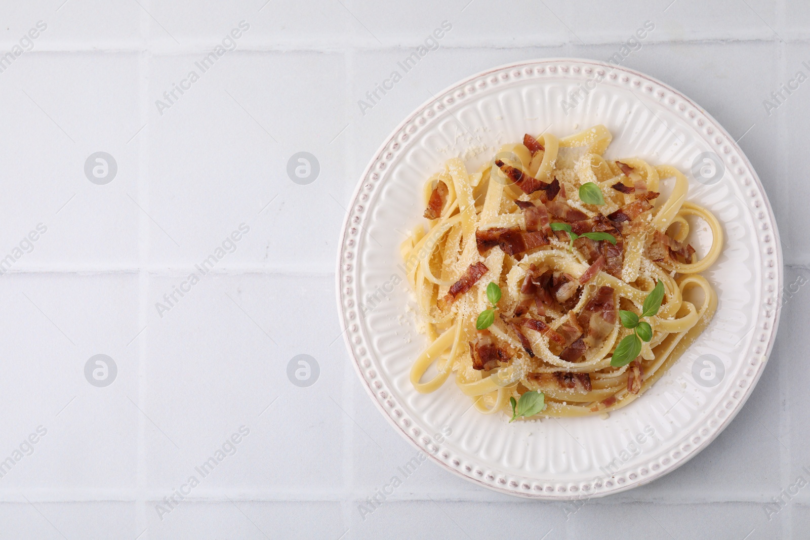 Photo of Tasty pasta with bacon and basil on white tiled table, top view. Space for text