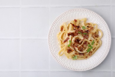 Tasty pasta with bacon and basil on white tiled table, top view. Space for text