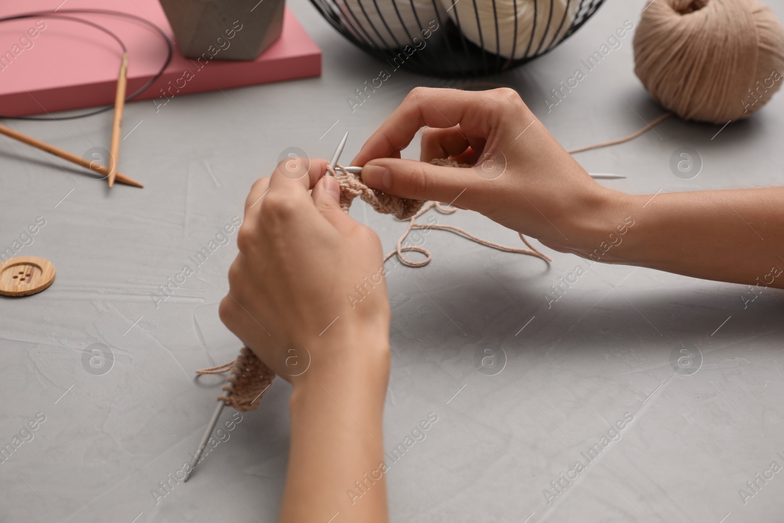 Photo of Woman knitting with threads at grey table, closeup. Engaging hobby