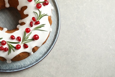Photo of Traditional Christmas cake decorated with glaze, pomegranate seeds, cranberries and rosemary on light grey table, top view. Space for text