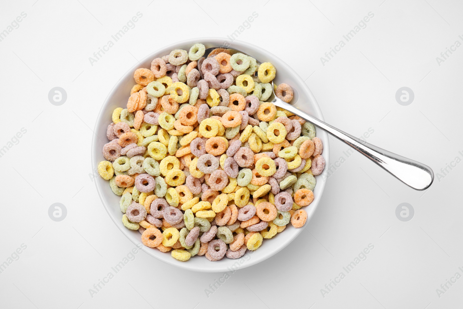 Photo of Tasty cereal rings in bowl and spoon on white table, top view