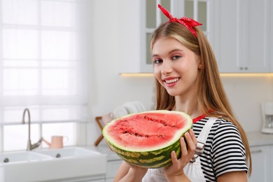 Beautiful teenage girl with half of watermelon in kitchen, space for text