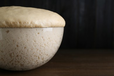 Photo of Bowl of fresh yeast dough on wooden table, closeup. Space for text