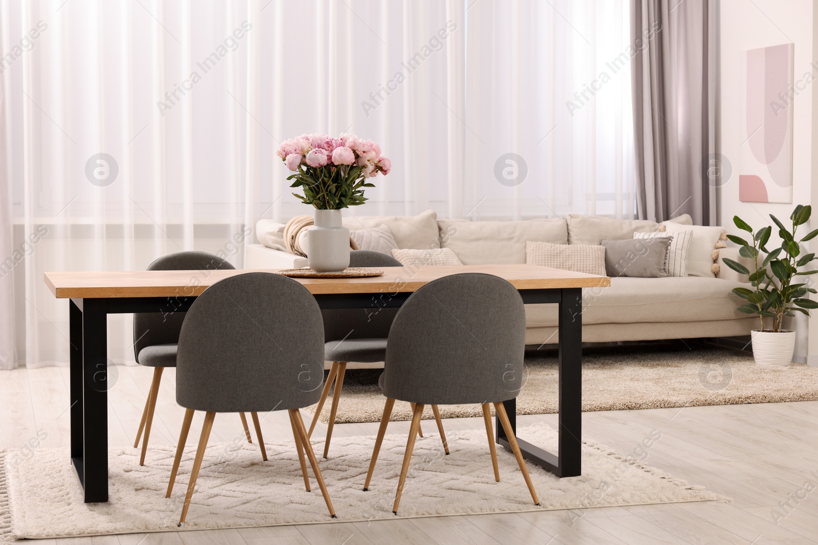 Photo of Table, chairs, sofa and vase with peonies in stylish dining room