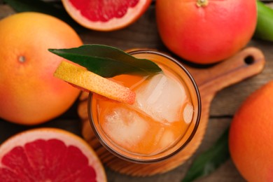 Photo of Tasty grapefruit drink with ice and leaf in glass surrounded by fresh fruits on wooden table, flat lay