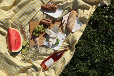 Picnic blanket with delicious food and wine on green grass outdoors, top view