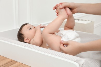 Mother changing baby's diaper on table at home, closeup