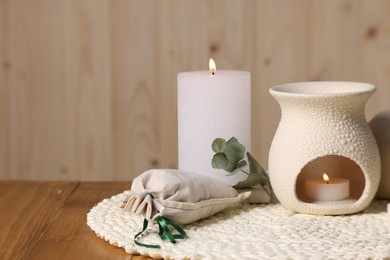 Aromatherapy. Burning candles and scented sachet on wooden table, closeup. Space for text