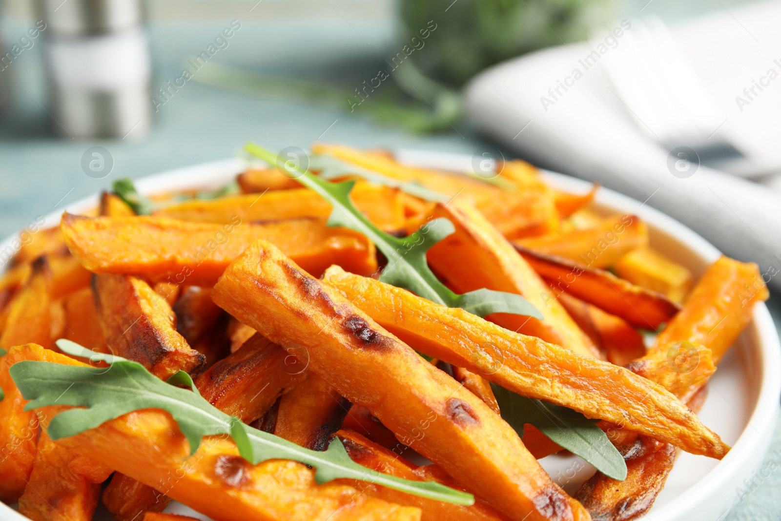 Photo of Plate with baked sweet potato slices and arugula on table, closeup