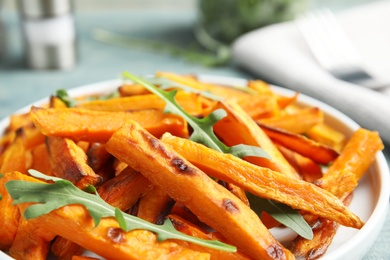 Plate with baked sweet potato slices and arugula on table, closeup