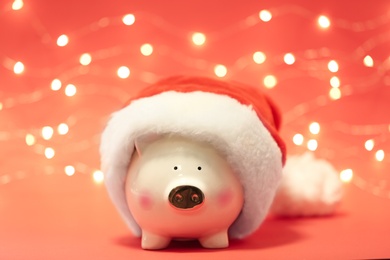 Photo of Cute piggy bank with Santa hat against blurred Christmas lights