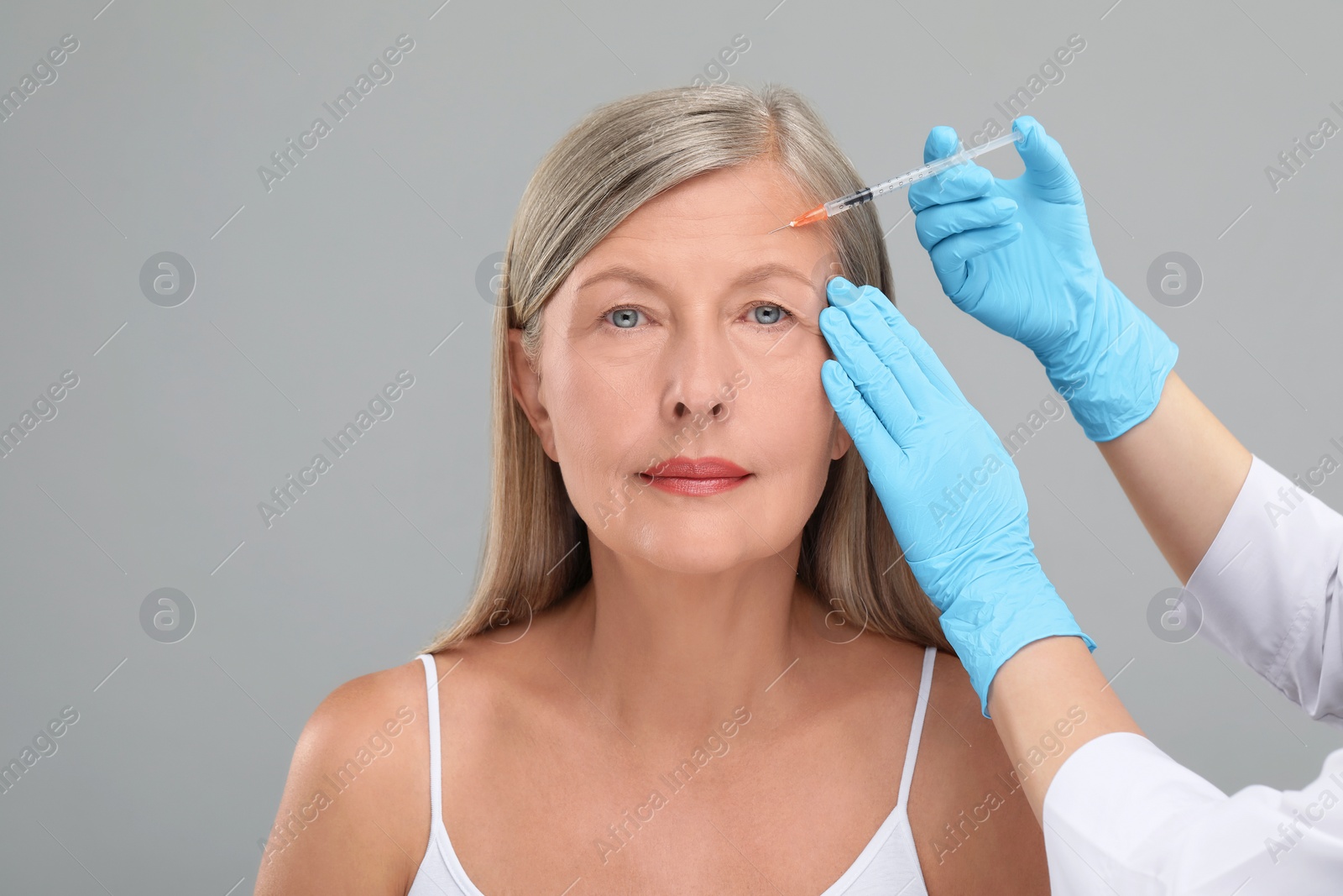 Photo of Doctor giving facial injection to senior woman on light grey background, closeup. Cosmetic surgery