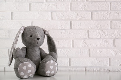 Photo of Stuffed bunny toy for baby room interior on table near white brick wall