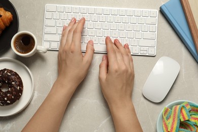 Photo of Bad eating habits. Woman working on computer at light grey marble table with different snacks, top view