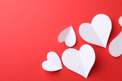 White paper hearts on red background, flat lay. Space for text