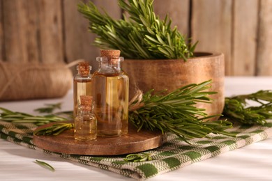 Photo of Essential oil in bottles and rosemary on white wooden table