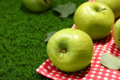 Photo of Ripe green apples and picnic blanket on grass, closeup. Space for text