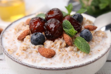 Photo of Tasty wheat porridge with milk, dates, blueberries and almonds in bowl, closeup