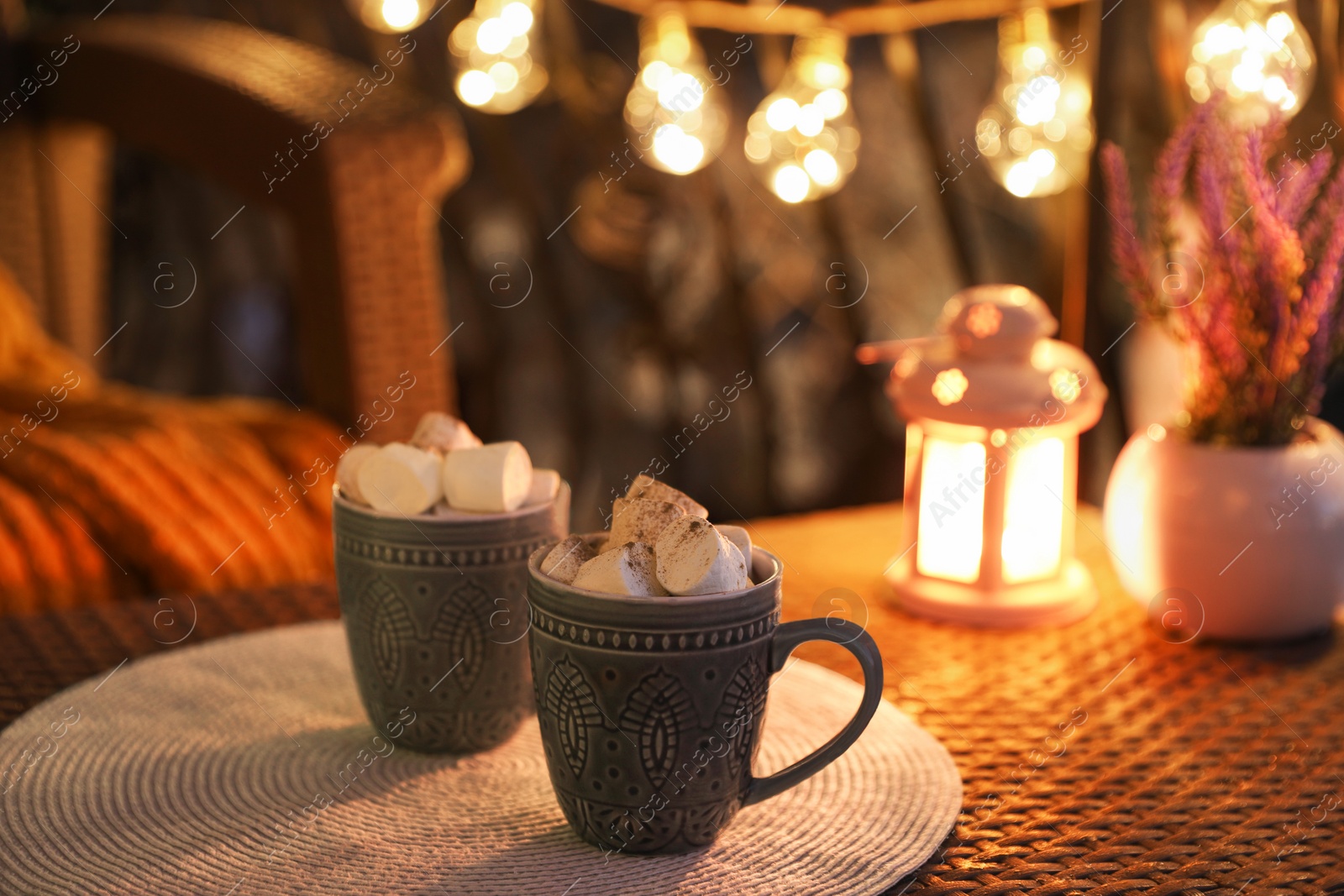 Photo of Cups with tasty cocoa and marshmallows on rattan table at balcony in evening