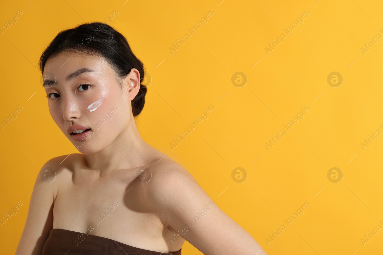 Photo of Beautiful young woman with sun protection cream on her face against orange background, space for text