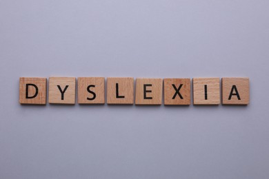 Wooden tiles with word Dyslexia on light grey background, flat lay