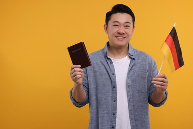 Photo of Immigration. Happy man with passport and flag of Germany on orange background, space for text