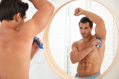 Handsome young man applying deodorant in bathroom