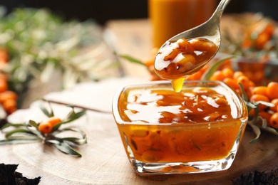 Photo of Spoon with delicious sea buckthorn jam over bowl, closeup. Space for text