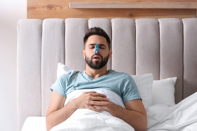 Photo of Man with clothespin suffering from runny nose in bed