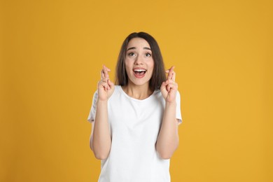 Photo of Excited young woman holding fingers crossed on yellow background. Superstition for good luck