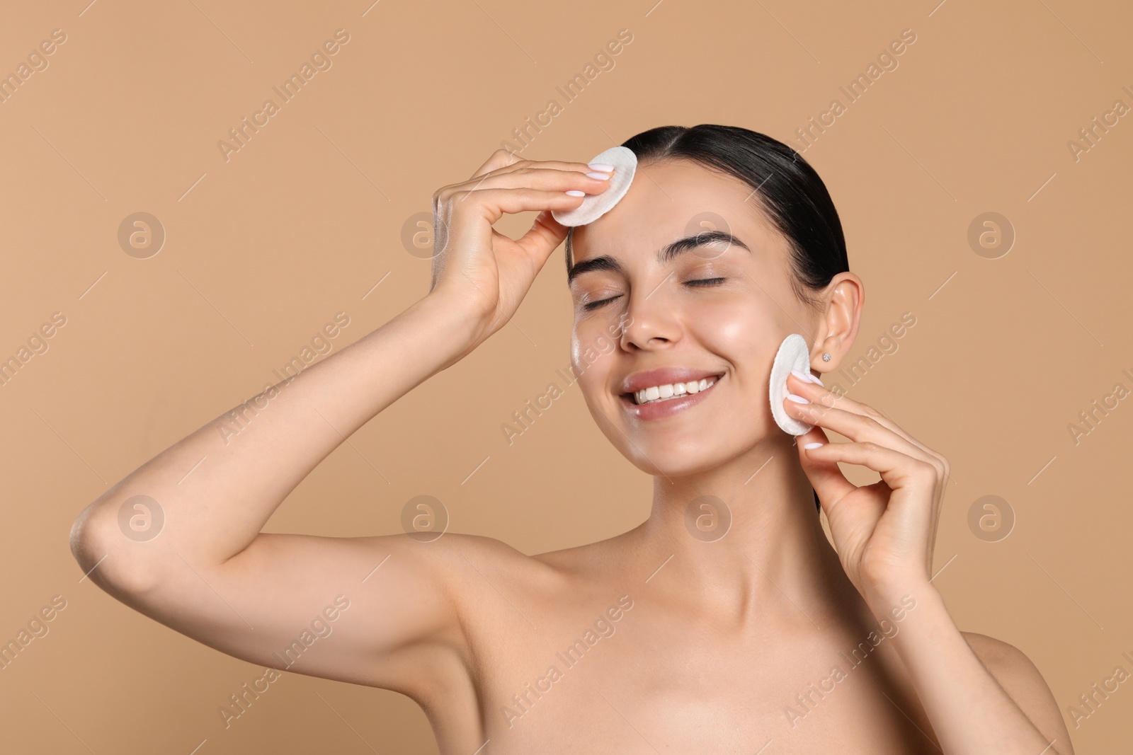 Photo of Young woman using cotton pads with micellar water on beige background