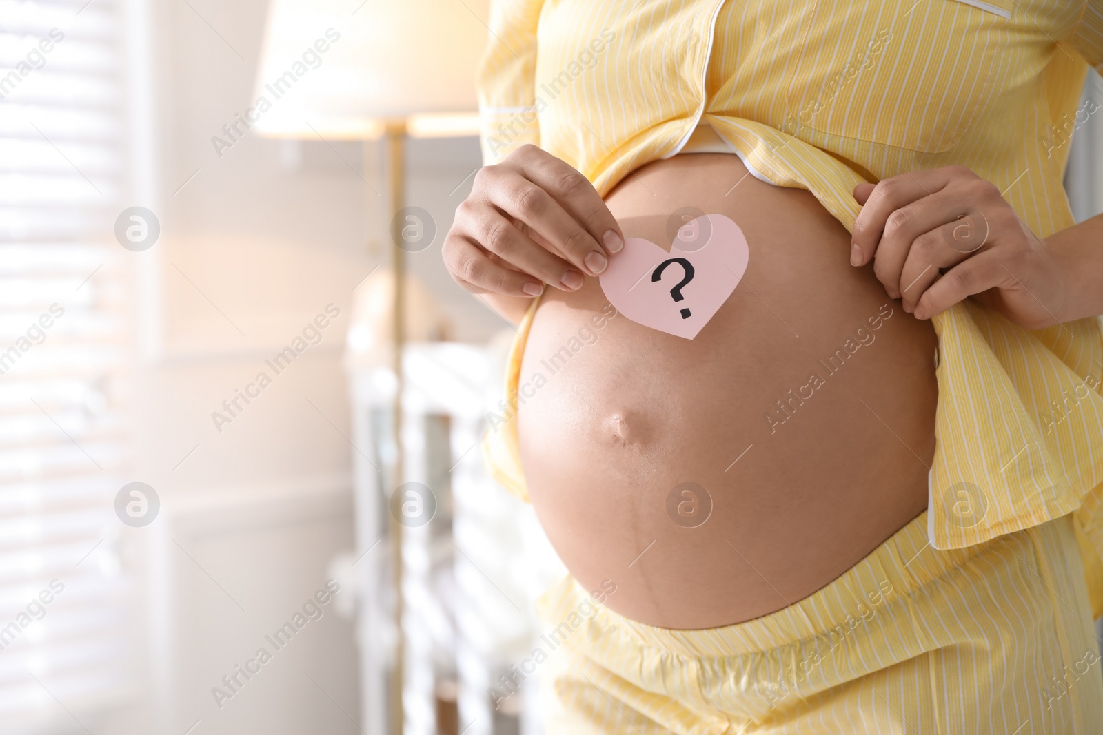 Photo of Pregnant woman with heart shaped sticky note on belly indoors, closeup. Choosing baby name