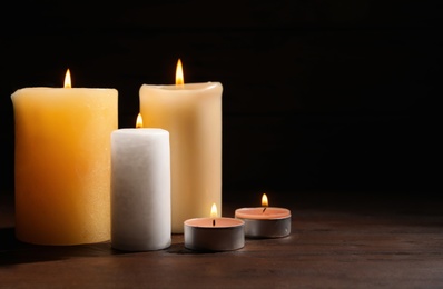 Different wax candles burning on table against dark background
