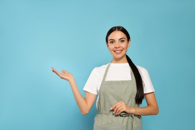 Young woman in grey apron on light blue background